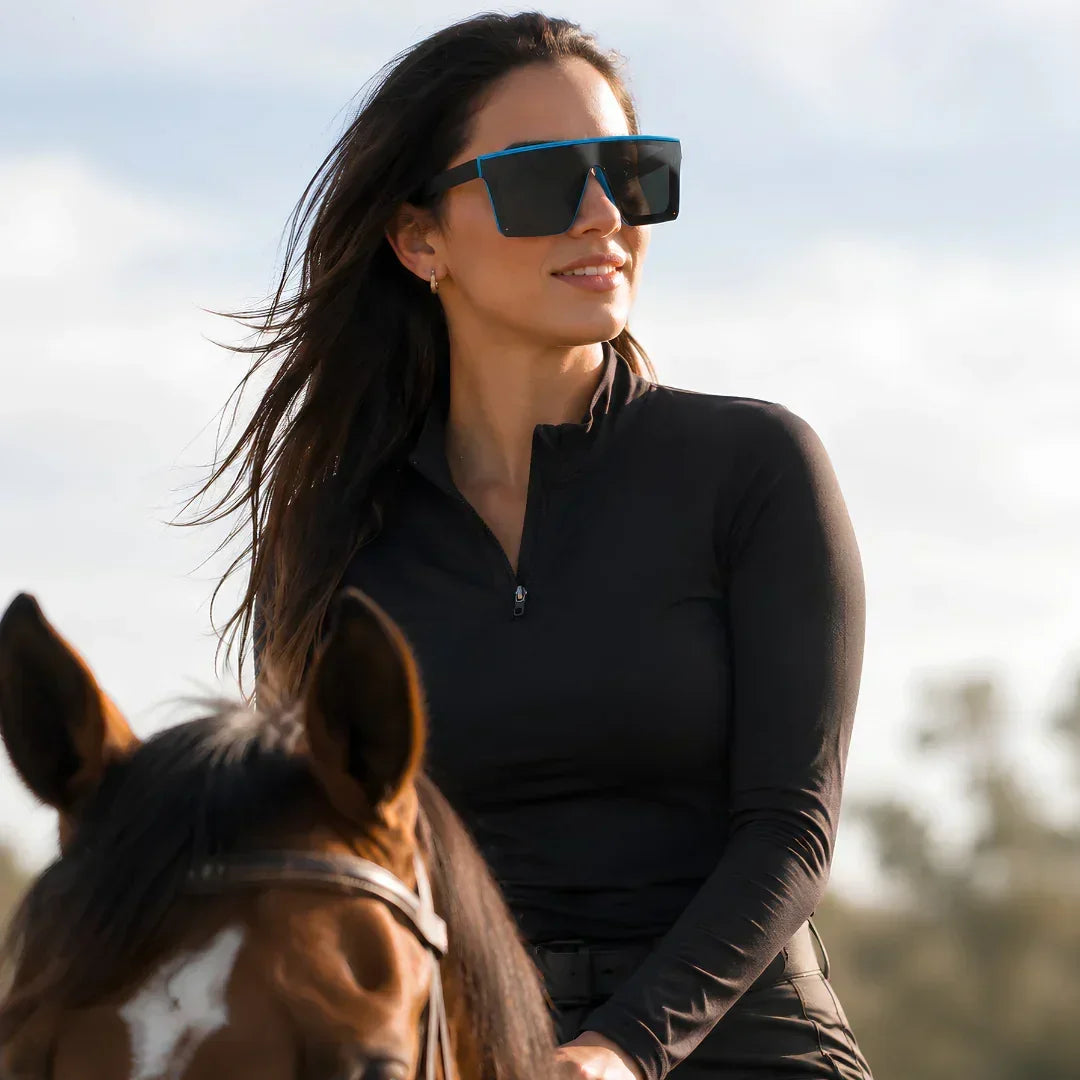Woman wearing stylish blue-frame sunglasses while horseback riding, UV protection, polarized lenses