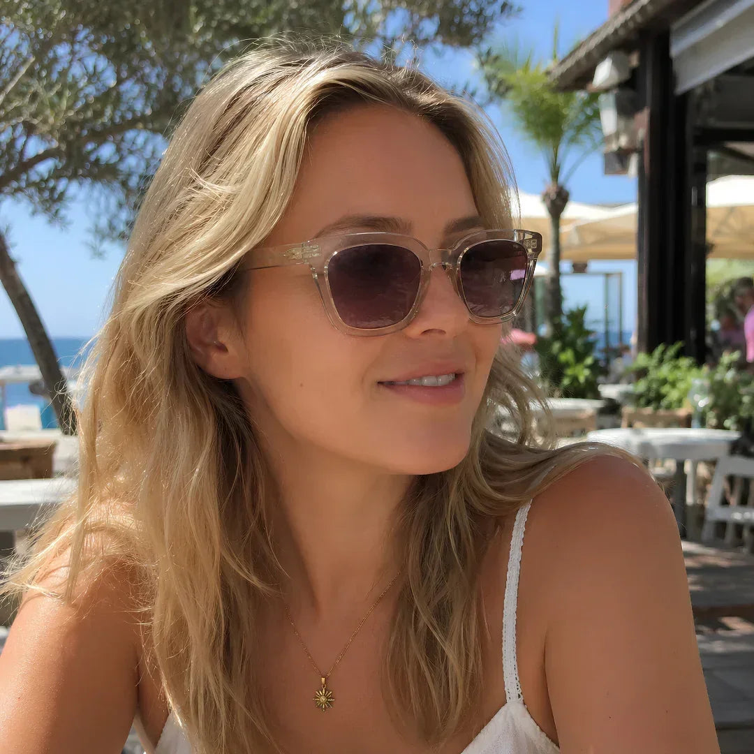 Woman wearing stylish square sunglasses with UV protection, enjoying sunny beachside cafe