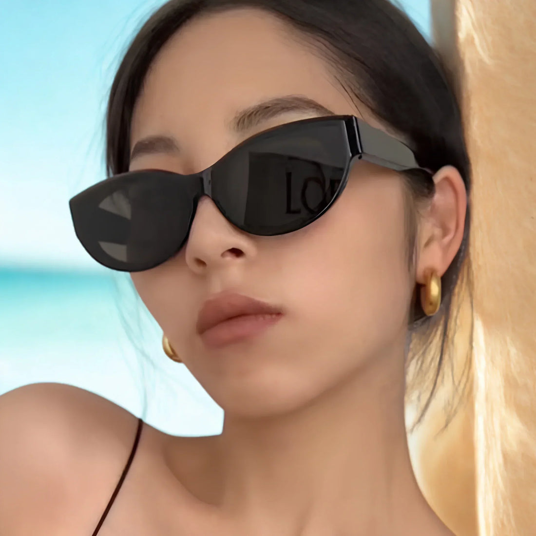 Stylish black cat-eye sunglasses with UV protection, worn by woman at beach, trendy luxury design
